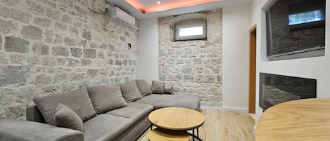 A modern living room with a stone wall, a sectional sofa, a round wooden table, and a fireplace.