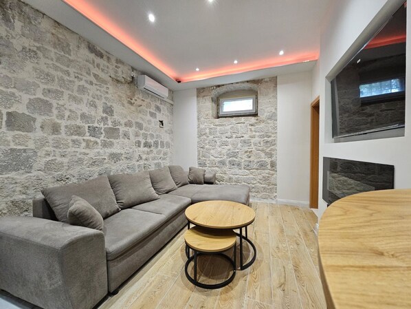 A modern living room with a stone wall, a sectional sofa, a round wooden table, and a fireplace.