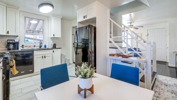 A modern kitchen with white cabinets, a black refrigerator, and a dining area with a white table and blue chairs. - Updated Arlington Townhome ~ 5 Mi to National Mall (Arlington)