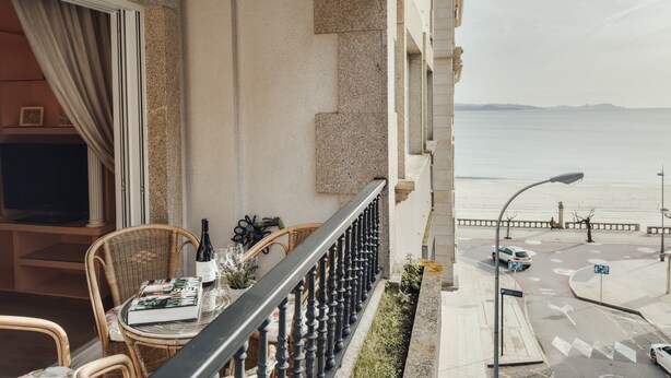 A balcony with a table set for dining, overlooking a beach and street. - Apartamento ThatsHome Silgar 4 (Sanxenxo)