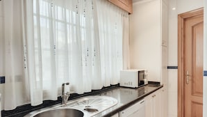 A kitchen with a stainless steel sink, a microwave, and white cabinets. - Apartamento ThatsHome Silgar 4 (Sanxenxo)