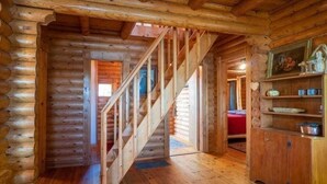 Et interiør af en træhytte med en trætrap, en rød seng og et træskab med dekorative genstande.