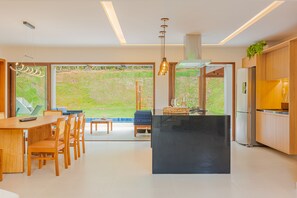 A modern kitchen with a central island, wooden dining area, and large windows offering a view of the outdoors.