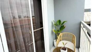 A balcony with a sliding glass door, a wicker chair, a small table, and a potted plant.