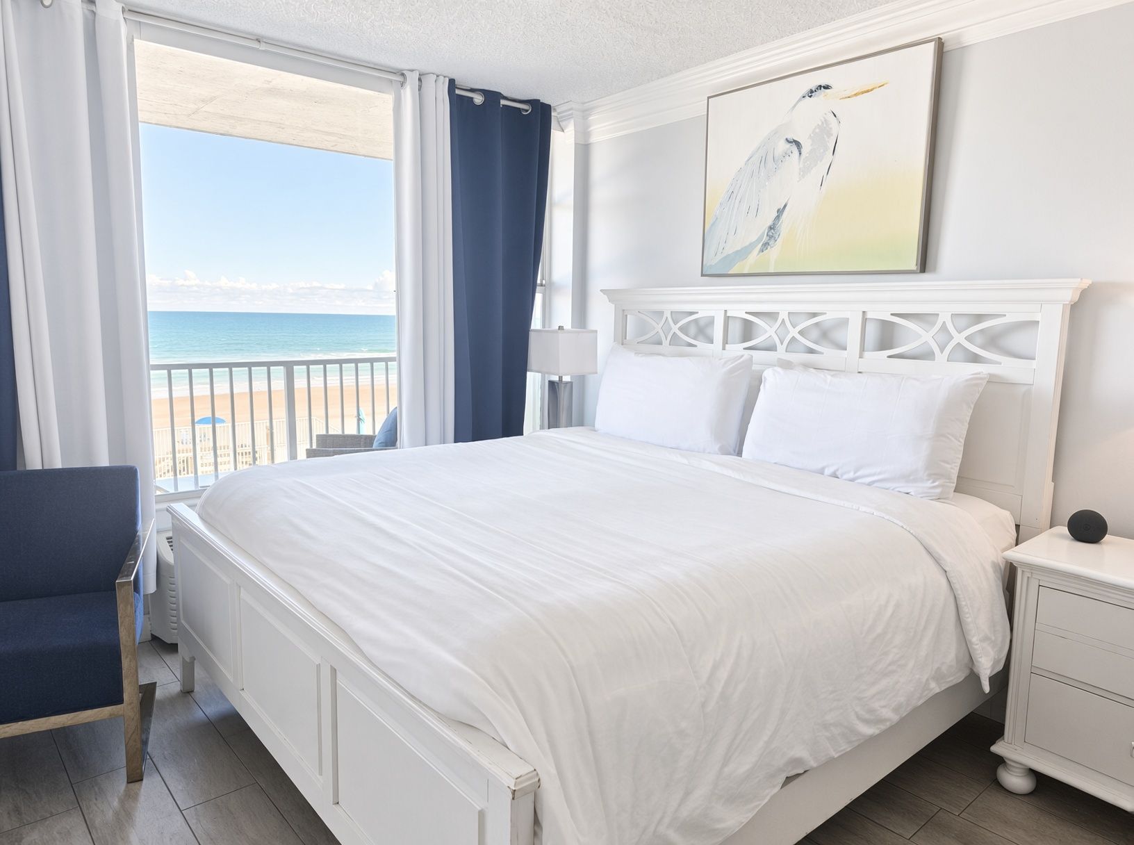 Een hotelkamer met een bed, een stoel, een nachtkastje, een lamp en een schilderij van een vogel.