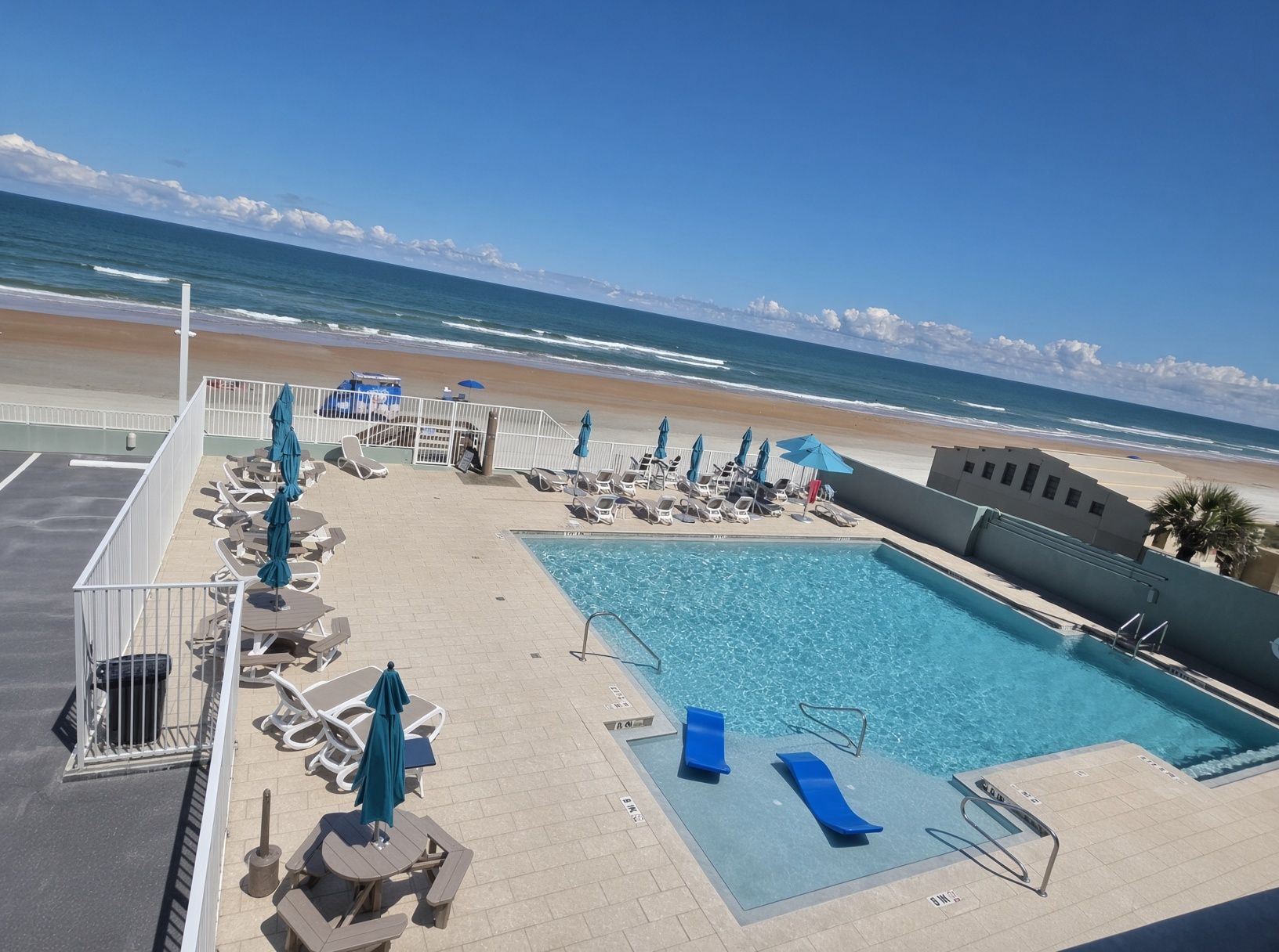 Een zwembad met ligbedden en parasols, met uitzicht op een strand en oceaan.
