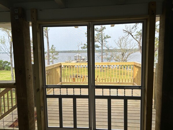 A wooden deck with a railing overlooking a lake, a dock, and a grassy area. - Secluded waterfront fishing cabin, boat dock, pier, sunsets, boat to beach (Foley)