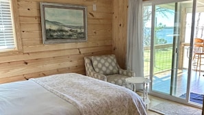 Ein Schlafzimmer mit Bett, Deckenventilator, Gemälde und Blick ins Freie.