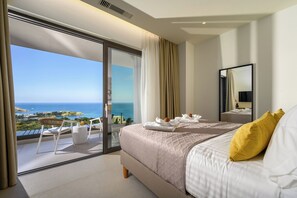 Habitación de hotel con cama, balcón con vista al mar y zona de comedor con mesa y sillas.