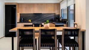 A modern kitchen with wooden cabinets, a black marble countertop, and a dining area with a wooden table and black chairs. - Kyma Majo Luxury Sea View Villa 6-Bedroom with Gym,Sauna,Heated Private Pool (Malevizi)