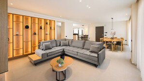 A modern living room with a sectional sofa, a wooden coffee table, and a dining area with a wooden table and chairs. - Kyma Majo Luxury Sea View Villa 6-Bedroom with Gym,Sauna,Heated Private Pool (Malevizi)