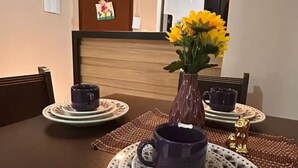 Et spisebord med en vase med gule blomster, to blå krus og mønstrede underlag.