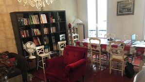Ein Wohnzimmer mit einem roten Sessel, einem Bücherregal, einem Esstisch mit Stühlen und einer Chandelüster.