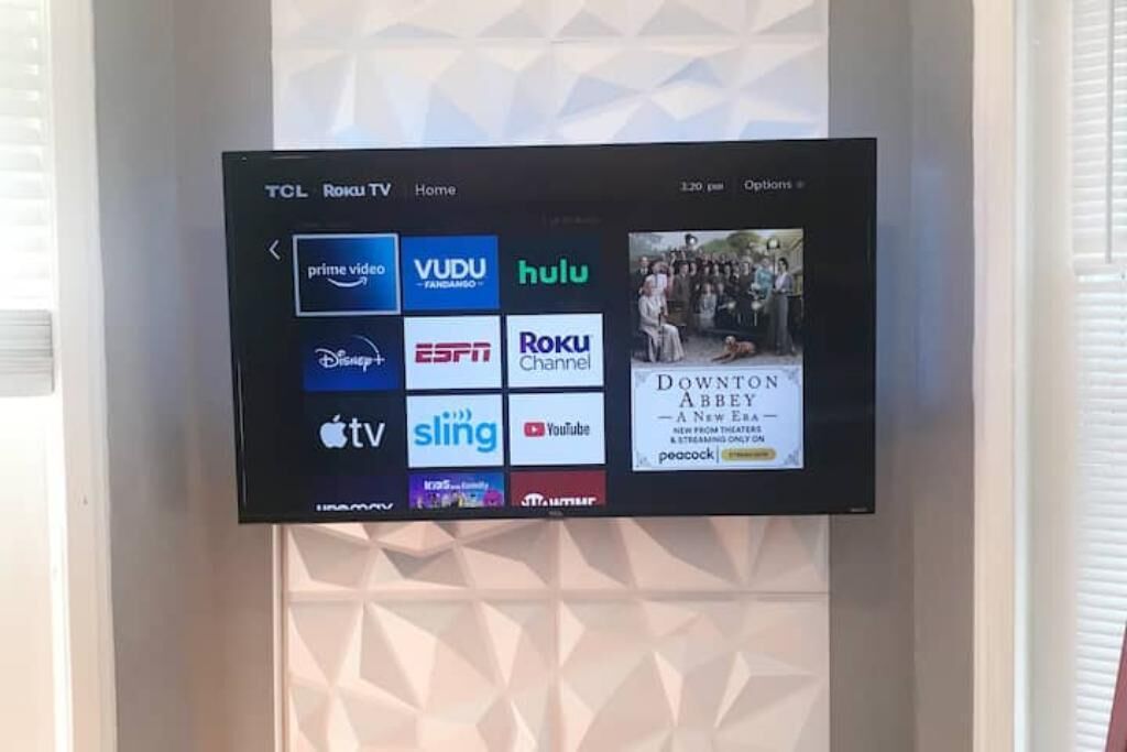 A TCL Roku TV mounted on a wall with a geometric pattern.