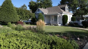 Une maison de plain-pied avec un porche à l’avant, entourée d’un jardin bien entretenu et d’arbres.