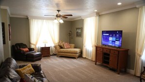 Un salon comprenant un canapé, un pouf, un téléviseur, un ventilateur de plafond et un meuble.