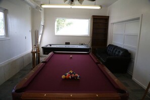 A pool table with balls, a pool cue, a sofa, and a window. - Updated Cottage Sleeps 8 Close to Logan (River Heights)