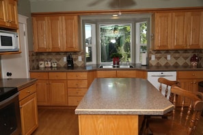 A kitchen with wooden cabinets, a granite countertop, a built-in microwave, and a window with a view of greenery. - Updated Cottage Sleeps 8 Close to Logan (River Heights)