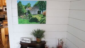 Un coin de pièce avec une table en bois, un tableau encadré, une plante en pot et un vase de fleurs.