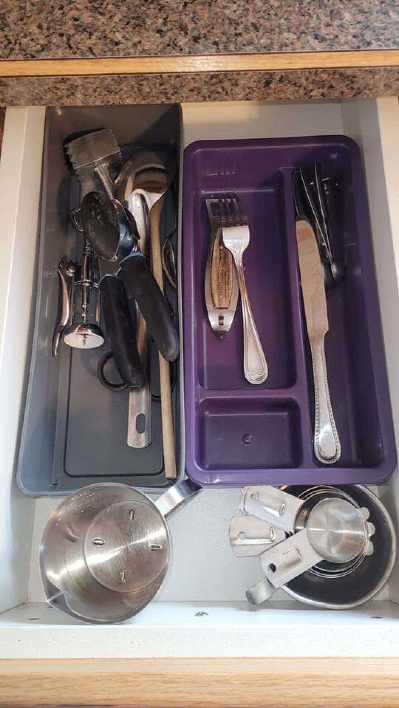 En låda med köksredskap och verktyg, inklusive en stekspade, gaffel, kniv och måttsatser.