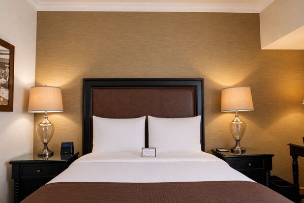 A hotel room with a large bed, two bedside tables, and two lamps.