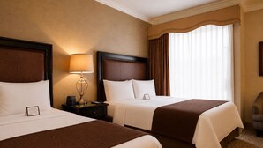 A hotel room with two beds, a nightstand with a lamp, a chair, and a large window with curtains. - The Inn at UCLA (Los Angeles)