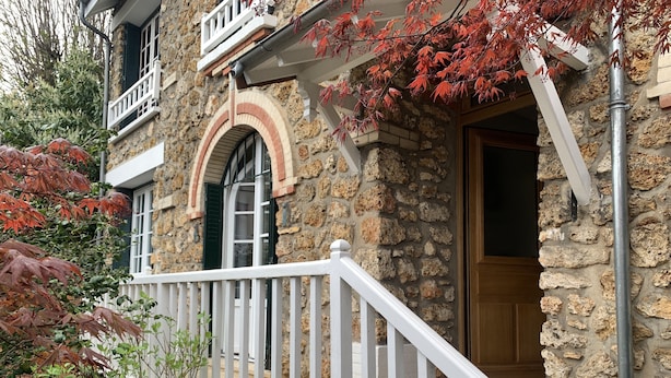 Ein Steinhaus mit weißem Balkon, einer Holztür und einem Fenster mit grünen Fensterläden.