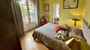 Ein Schlafzimmer mit Bett, einer Kandelaber, einer Lampe, einem Gemälde und Blick durch ein Fenster.