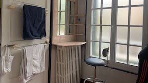 Ein Badezimmer mit einer weißen Tür, einem Handtuchhalter mit einem blauen Handtuch, einem weißen Handtuch, einem Spiegel, einem Heizkörper, einem Fenster mit Milchglas und einem Stuhl.