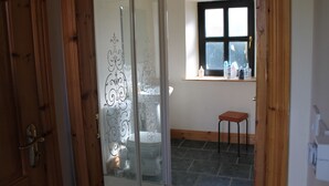 A room with a sliding glass door leading to a bathroom, a small stool near a window, and a shelf with toiletries.