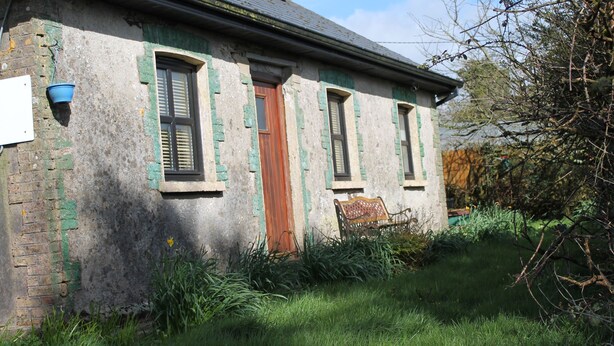 A rustic building with a wooden door, a bench, and a hanging bucket.