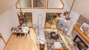 Amplio espacio tipo loft con techo alto, ventanas grandes, comedor, sofá, chimenea y televisor.