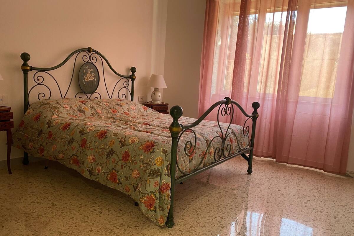A bedroom with a bed, a nightstand, a lamp, and a window with curtains.