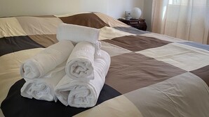 A neatly made bed with rolled white towels, a dark brown and beige quilt, and a nightstand with a lamp. - B&B POSEIDON (Fiumicino)