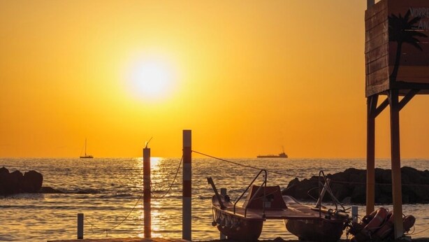 A wooden pier leading to a beach with boats and a lifeguard tower at sunset. - B&B POSEIDON (Fiumicino)