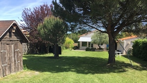Une cour bien entretenue, recouverte d’herbe, avec un abri en bois, un grand arbre et une maison dont le toit rouge se détache à l’arrière-plan.