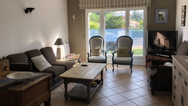 Un salon comprenant un canapé, deux fauteuils, une table basse, un téléviseur et une grande fenêtre donnant sur l’extérieur.
