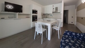 Une cuisine moderne avec des meubles blancs, un four encastré et un four à micro-ondes. On y trouve également un coin repas avec une table et des chaises blanches.