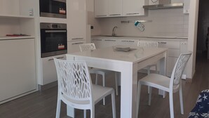Une cuisine moderne avec des meubles blancs, un four en acier inoxydable et un coin repas comprenant une table et des chaises blanches.