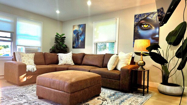 A modern living room with a brown sectional sofa, a patterned rug, and a large abstract painting on the wall. - Updated 3Bedroom. 5beds group ready.Walk to the Casino and play game of Pool. (Springfield)