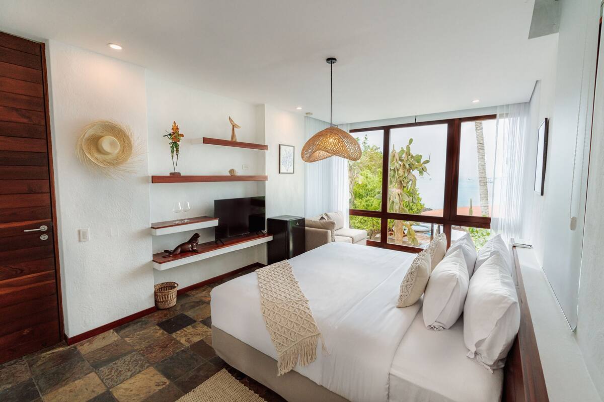 A modern bedroom with a large bed, wooden shelves, a television, and a view of greenery outside.