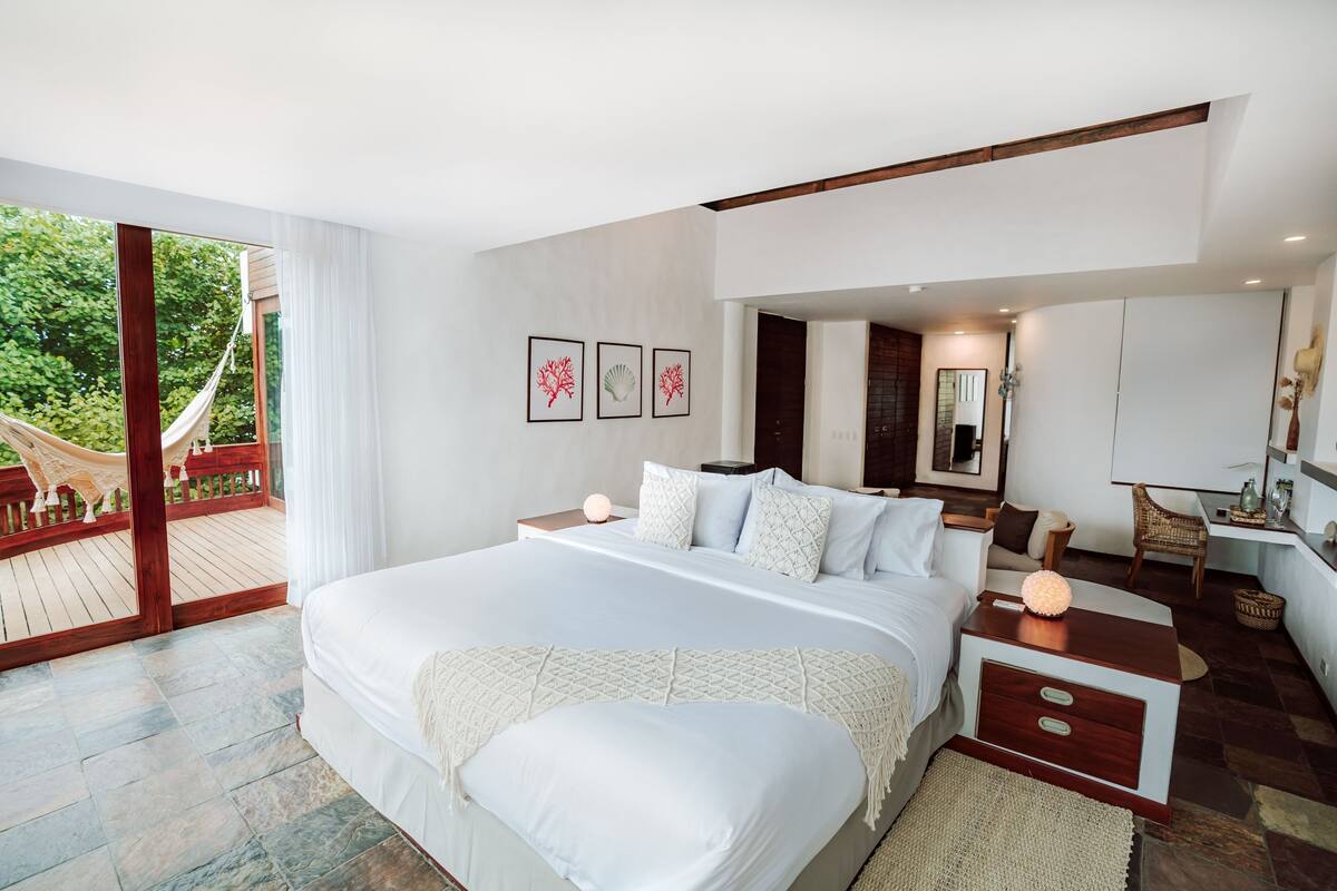 A modern bedroom with a large bed, a wooden nightstand, a small table, and a view of a wooden deck.