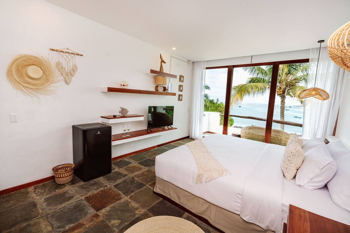 A modern hotel room with a large bed, a TV, and a view of the ocean.