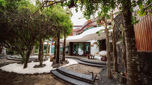 A modern building with a curved balcony, surrounded by a garden with trees and a stone pathway. - Hotel Villa Escalesia Galapagos (Puerto Ayora)