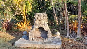 A stone structure with a central opening, surrounded by a grassy area with scattered leaves. - PARADISE CREEK COTTAGES (Andros Town)