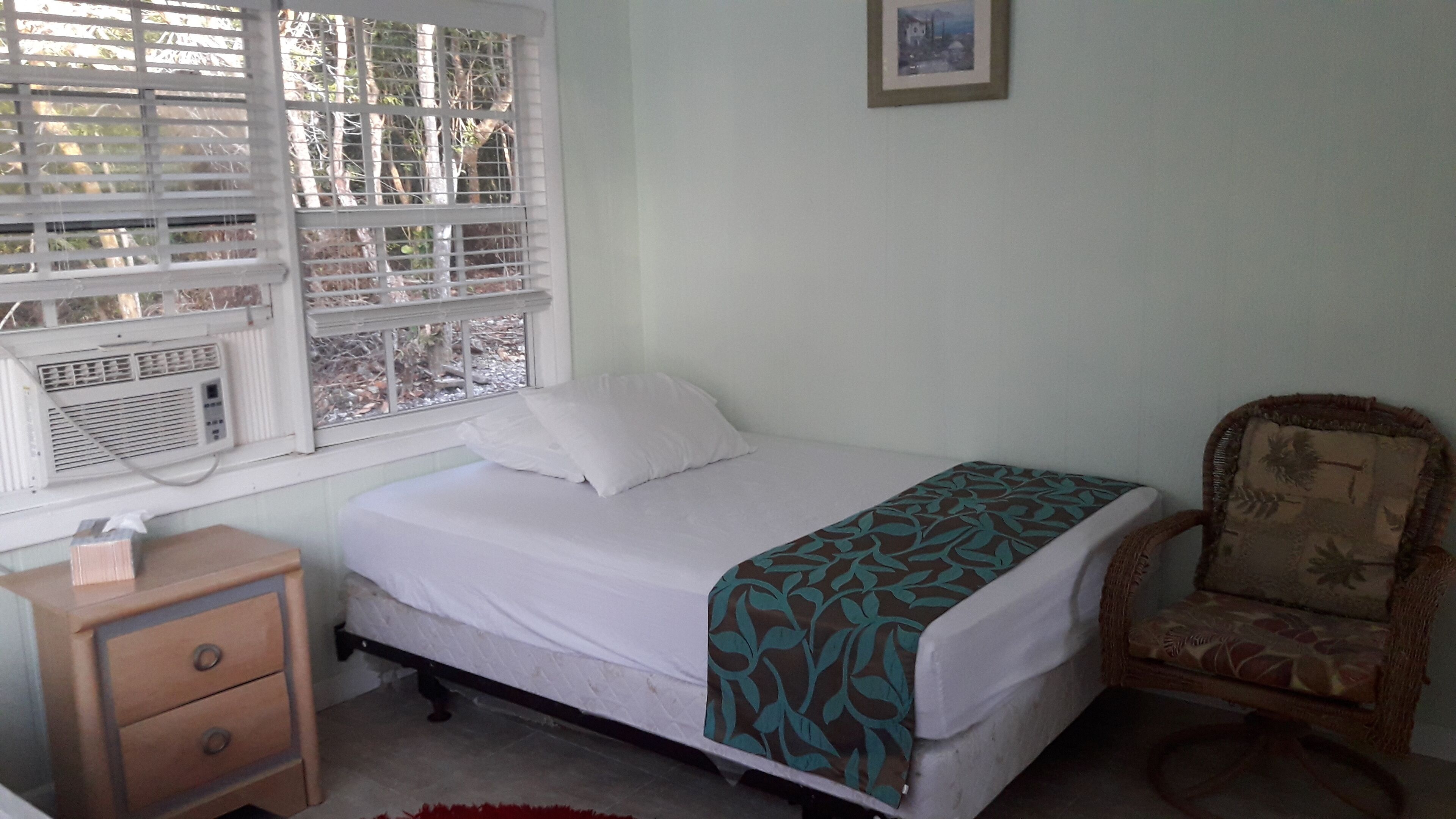 Un dormitorio con cama, mesita de noche, silla y ventana con persianas.