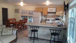 A compact kitchen with a refrigerator, microwave, stove, and bar stools. - PARADISE CREEK COTTAGES (Andros Town)