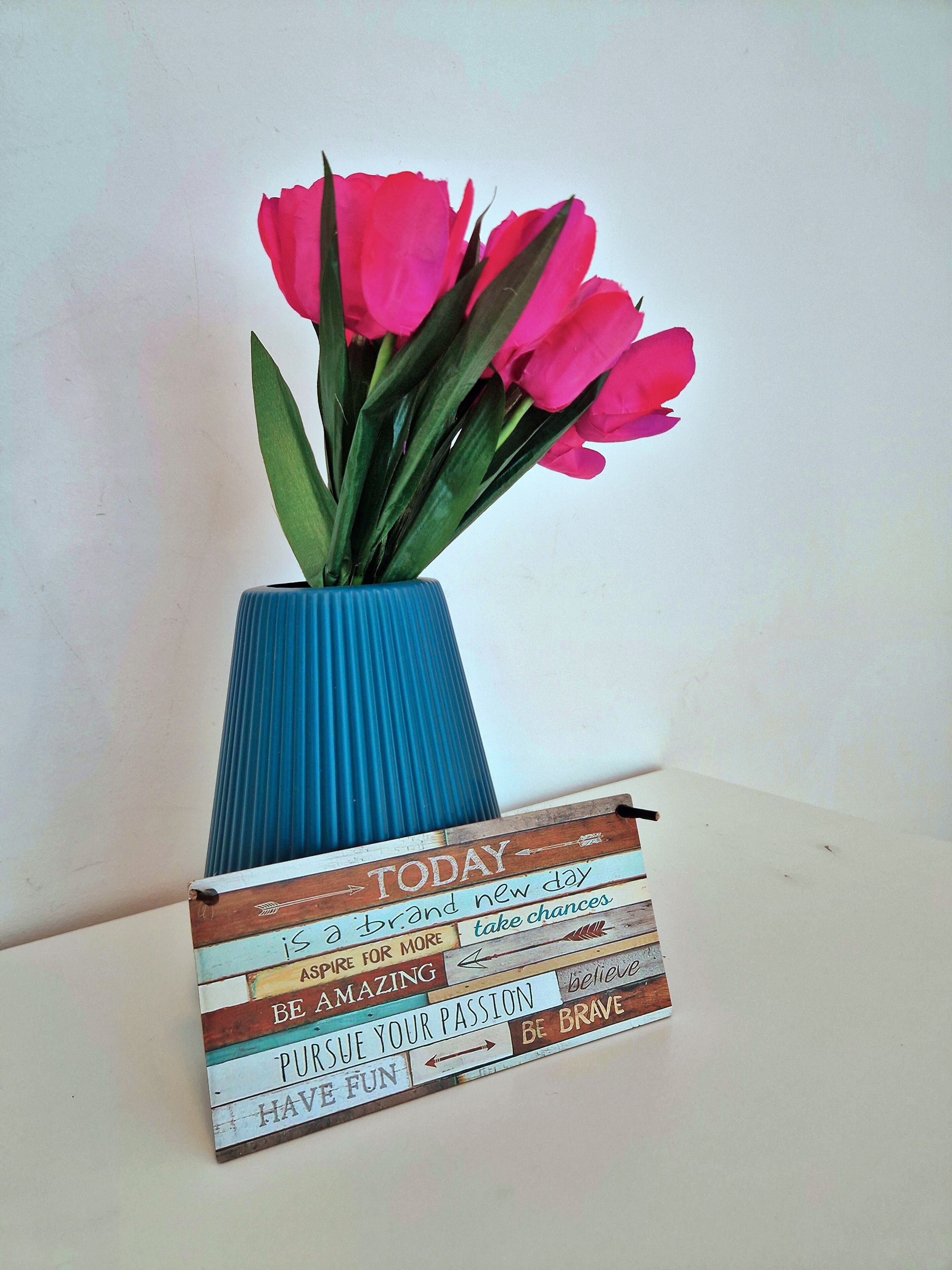 A blue vase with pink flowers and a motivational quote sign.