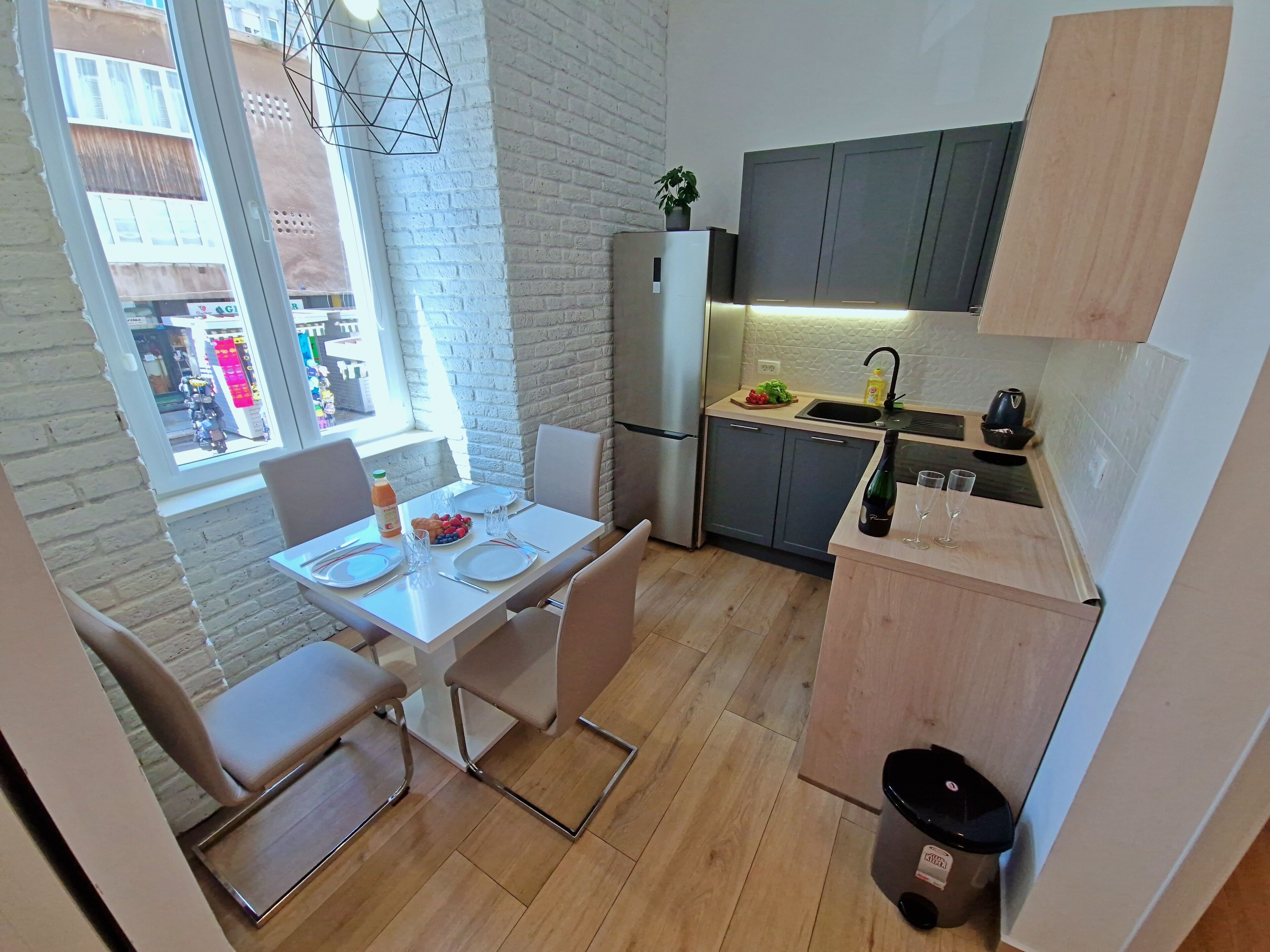 A compact kitchen with a dining area, a refrigerator, a sink, and a window overlooking a street.