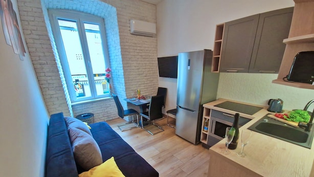 Een compact woongedeelte met een kitchenette, een eethoek en een bank met een geel kussen.